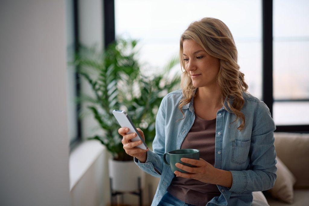 Woman checking auto loan rates on phone while drinking coffee at home in Springfield MO