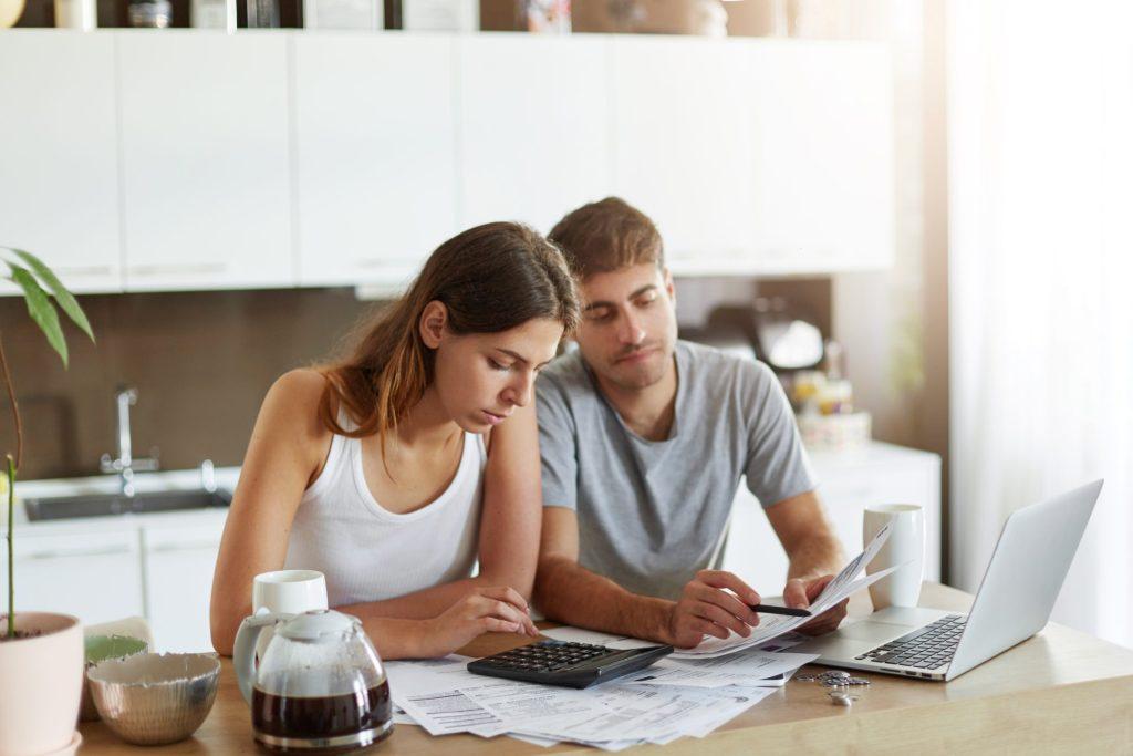 Couple reviewing finances and using a calculator to plan home affordability and mortgage budget at kitchen table