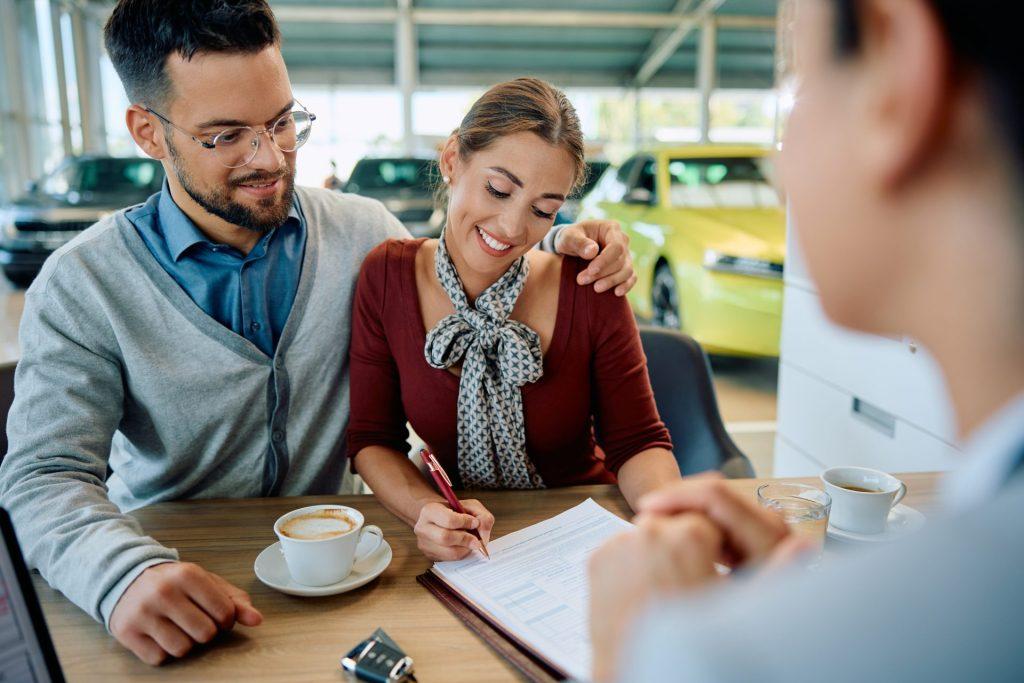Couple meeting with a loan advisor while discussing auto financing options at a car dealership showroom